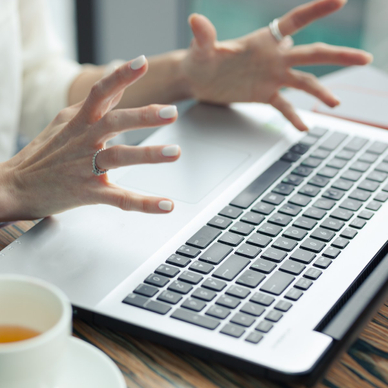A close-up photo of a woman&#x27;s tensed hands raised above her laptop keyboard to signify a slow computer