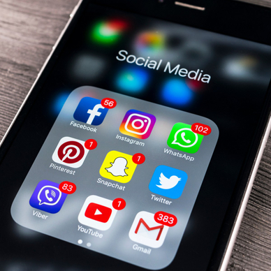 A close-up photo of an Apple iPhone 7 with a Social Media folder open and icons for Facebook, Instagram, WhatsApp, Pinterest, Snapchat, Twitter, Viber, YouTube, and Gmail all displayed.