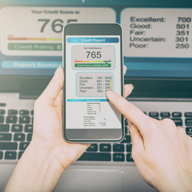 A man&#x27;s hands hold up a cell phone that shows a 765 credit score, intended to show the idea of credit monitoring and how it&#x27;s important to noticing and protecting yourself against identity theft.
