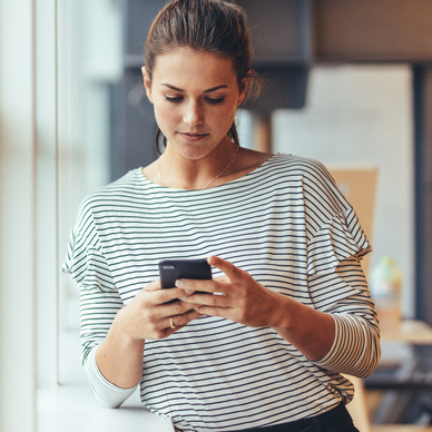 A woman leans against a doorframe while she uses a smartphone