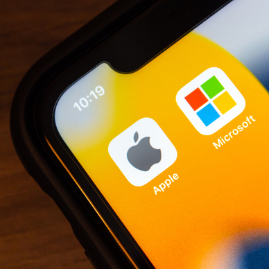 A close-up of a smartphone screen showing the logo for Apple next to the logo for Microsoft to represent Mac vs. PC.