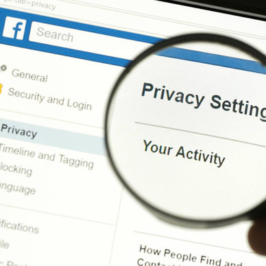 Hand holding a magnifying glass and magnifying the word &quot;Privacy settings&quot; on Facebook.