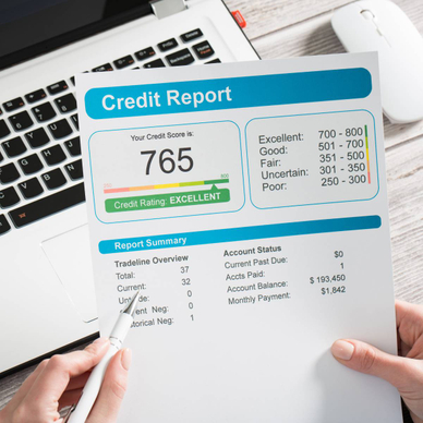Someone reviewing a print copy of their credit report over their laptop.