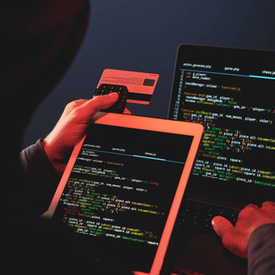 A hooded internet criminal is hacking a laptop in the dark and stealing credit card details.