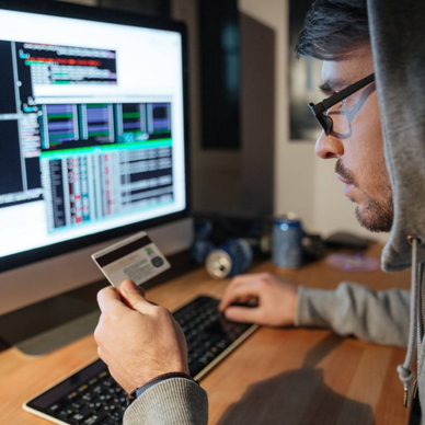 A hooded hacker is stealing money from different credit cards on their computer.