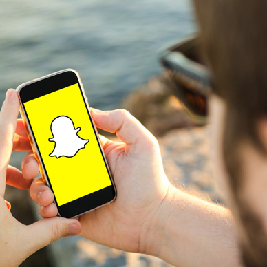 A man sits on the beach and uses his cell phone to access Snapchat.
