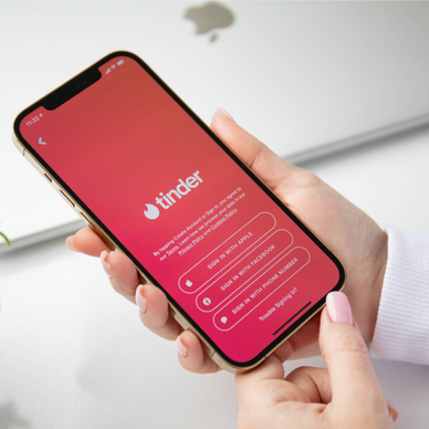 A woman&#x27;s hands holding an iPhone on the Tinder app login screen.
