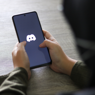 A close-up view of a woman holding a cell phone with the Discord app logo displayed.