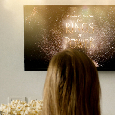 back of the head of a woman having popcorn watching The Lord of The Rings on TV