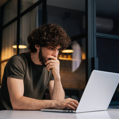 A young man sitting at his kitchen table while working on his laptop.