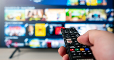 A hand shown holding a remote that&#x27;s pointed at a TV. 