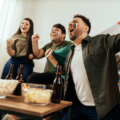Two men and a woman with face paint and a Mexican flag cheering with beer and popcorn in the living room