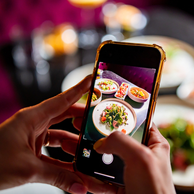 A closeup of a person holding their cell phone to take a photo of food at a restaurant.