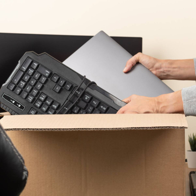 Woman placing an old laptop and keyboard in a cardboard box for recycling. 