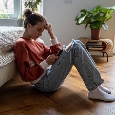 A teen girl sitting on the floor while using her smartphone. 