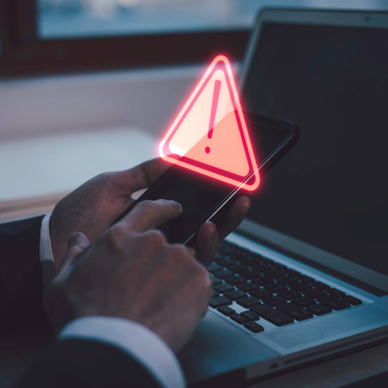 A man holding his smartphone in front of his laptop. There&#x27;s abstract warning above his phone.