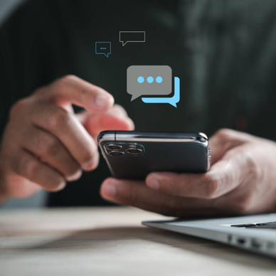 Man using his smartphone while sitting in front of his laptop with abstract text bubbles hovering above the phone.