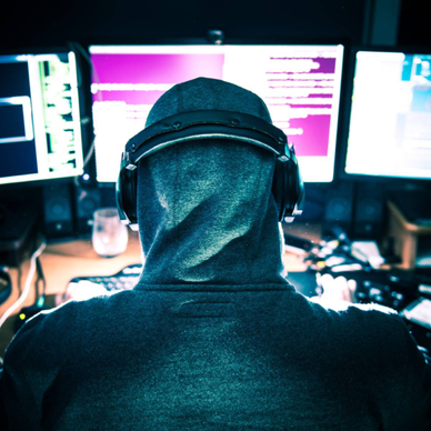 A hooded hacker viewing three computer monitors. 