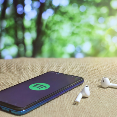 A smartphone displaying the Spotify app next to wireless buds