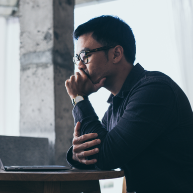 A man sits in front of his computer, resting his chin in his hand.