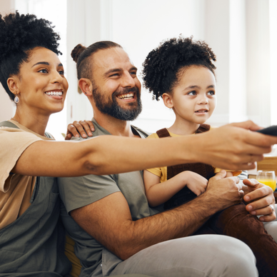 A family of three sits on the couch and watches TV.