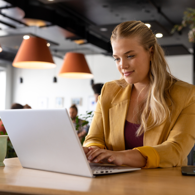 A woman sits at a desk and types on a laptop. 