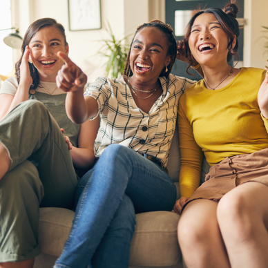 Three friends watch TV and laugh while sitting on the couch.