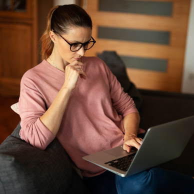 A woman sits on her couch while using her laptop. 