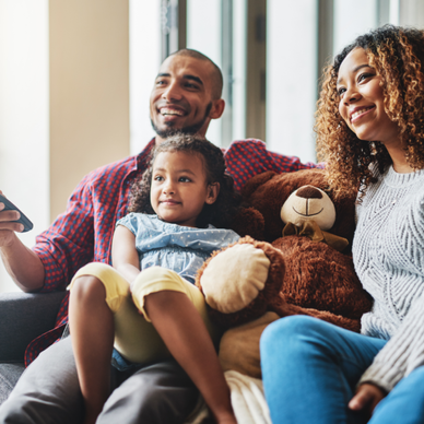 A family of three watch TV together on the couch.