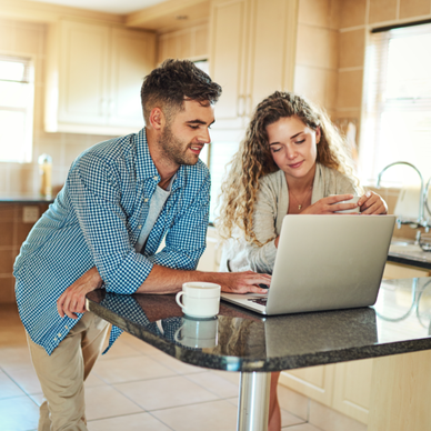A couple uses their laptop together in the kitchen for online banking.
