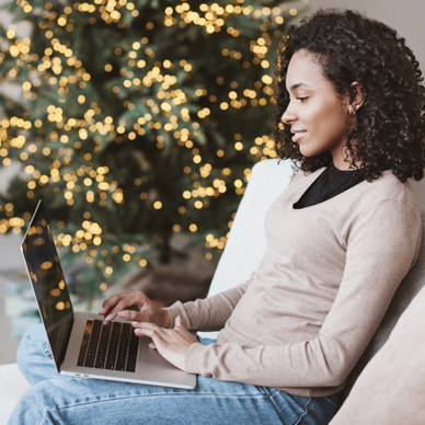 A woman uses a laptop on her couch with a Christmas tree behind her.