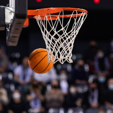 A closeup of a basketball swishing passed the net in a packed stadium