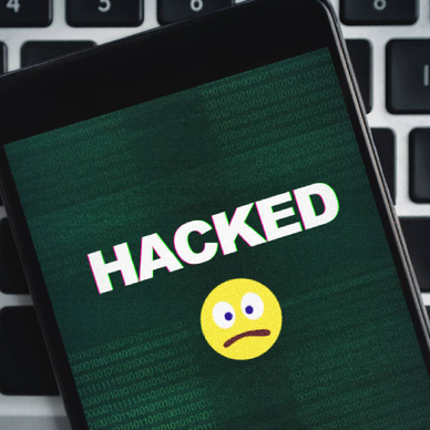 Closeup of a smartphone with a sad emoji and the word Hacked in all caps