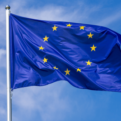 Flag of the European Union waving in the wind on flagpole against the sky with clouds on sunny day.