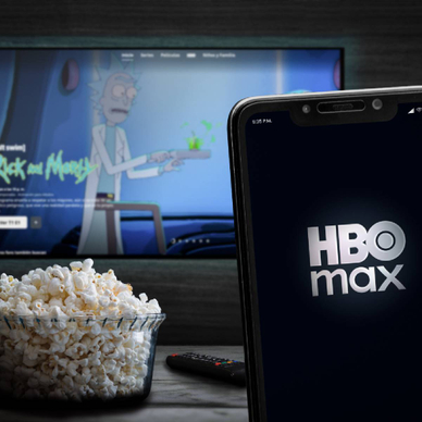 Smartphone displaying HBO Max in front of TV showing Rick and Morty and a bowl of popcorn
