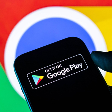 Closeup of a hand holding a smartphone displaying the Google Play Store logo against a Google Chrome background.