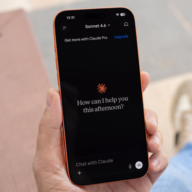 Hand holding cell phone with a new Claude chat opened on the screen.